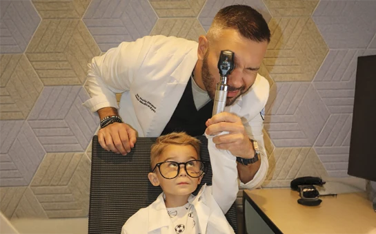 Dr. Haris Dzubur guides a child during an eye examination using a handheld vision tool.