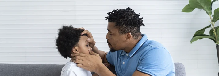 A man gently examines a child’s eyes in a bright setting, providing attentive and supportive care.